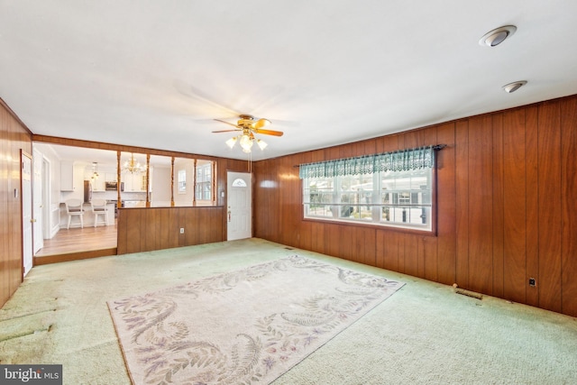 unfurnished living room with light colored carpet, ceiling fan, and wood walls