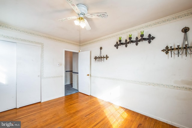 unfurnished bedroom featuring wood-type flooring, ornamental molding, a closet, and ceiling fan