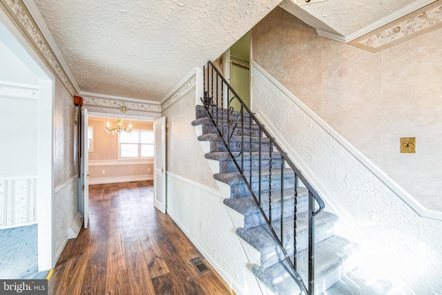 staircase with an inviting chandelier, crown molding, hardwood / wood-style floors, and a textured ceiling