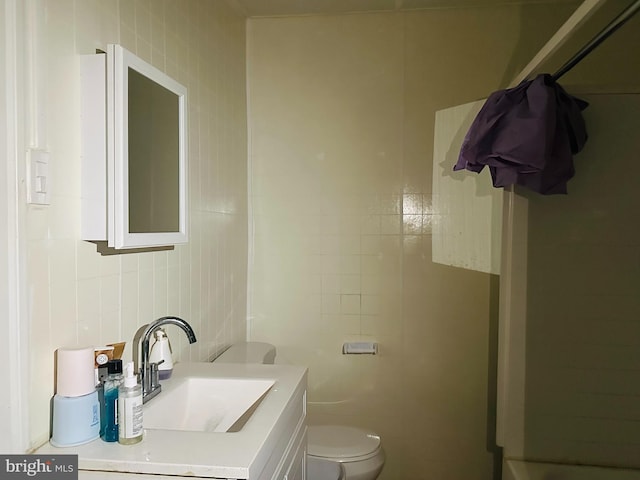 bathroom featuring vanity, tile walls, and toilet