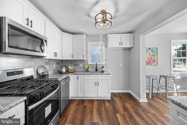 kitchen with stainless steel appliances, light stone countertops, sink, and white cabinets