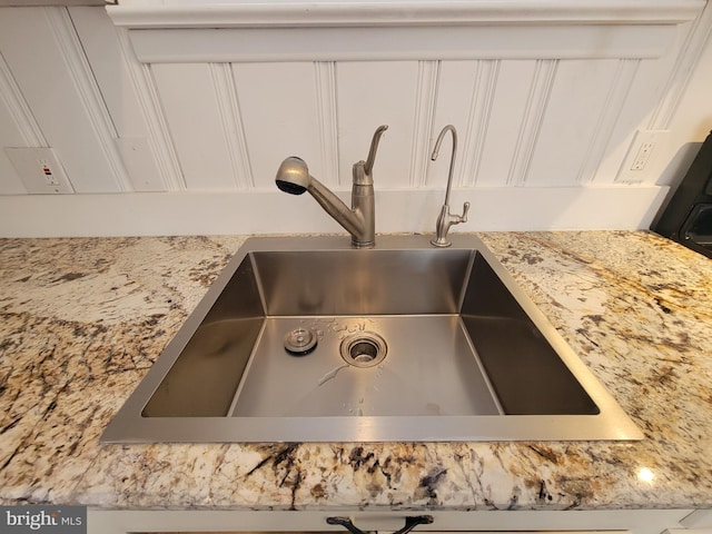 room details featuring white cabinetry, sink, and light stone counters