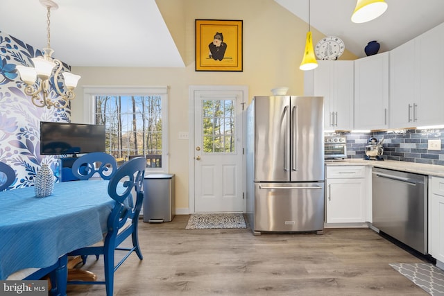 kitchen featuring pendant lighting, backsplash, stainless steel appliances, white cabinets, and vaulted ceiling