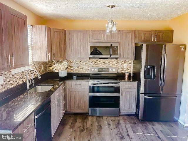 kitchen with decorative light fixtures, sink, dark stone countertops, stainless steel appliances, and dark wood-type flooring