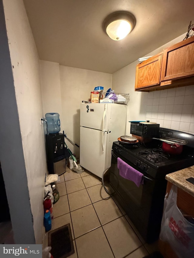 kitchen with tasteful backsplash, light tile patterned flooring, white fridge, and black gas range