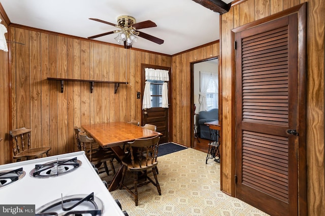 dining space with crown molding, ceiling fan, and wood walls