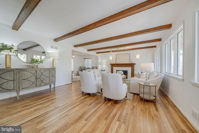 living room featuring visible vents, baseboards, a lit fireplace, beam ceiling, and light wood finished floors