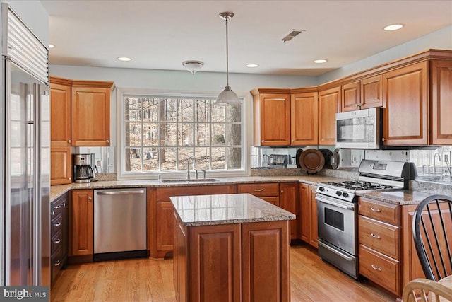 kitchen featuring pendant lighting, sink, a center island, stainless steel appliances, and light stone countertops