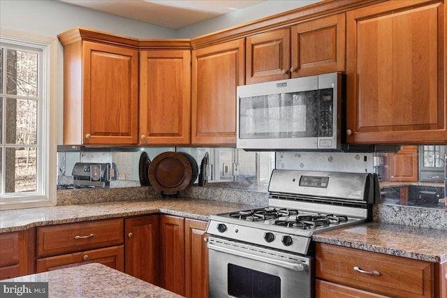 kitchen featuring tasteful backsplash, light stone countertops, a healthy amount of sunlight, and appliances with stainless steel finishes