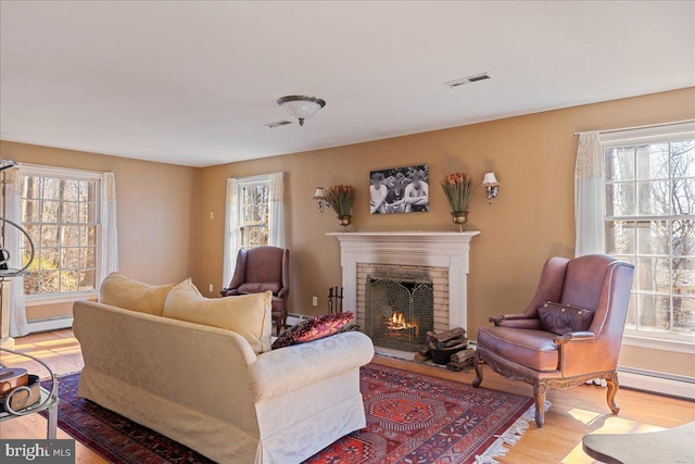 living room featuring a baseboard radiator, a brick fireplace, and light wood-type flooring