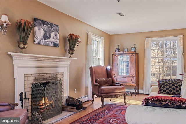 living area featuring wood-type flooring, a baseboard heating unit, and a fireplace