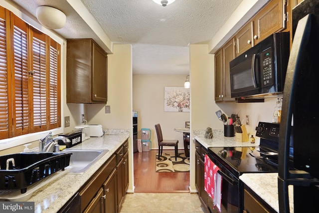 kitchen featuring decorative light fixtures, sink, black appliances, light stone countertops, and a textured ceiling