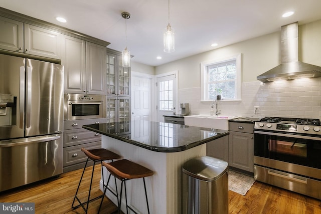 kitchen with gray cabinets, a kitchen island, a breakfast bar area, stainless steel appliances, and wall chimney exhaust hood