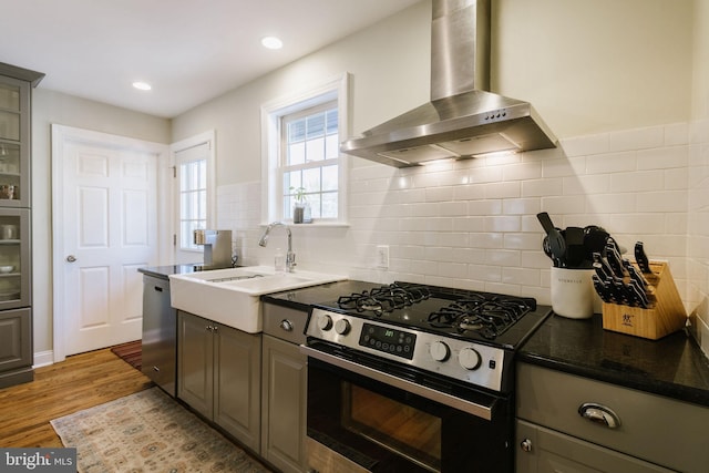 kitchen featuring sink, light hardwood / wood-style flooring, appliances with stainless steel finishes, gray cabinets, and wall chimney range hood