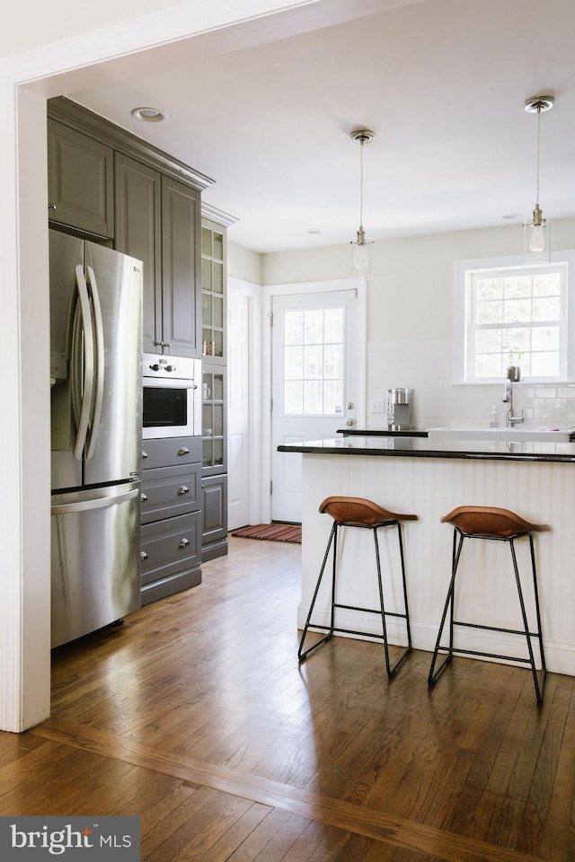 kitchen with gray cabinetry, a kitchen breakfast bar, oven, and stainless steel refrigerator with ice dispenser