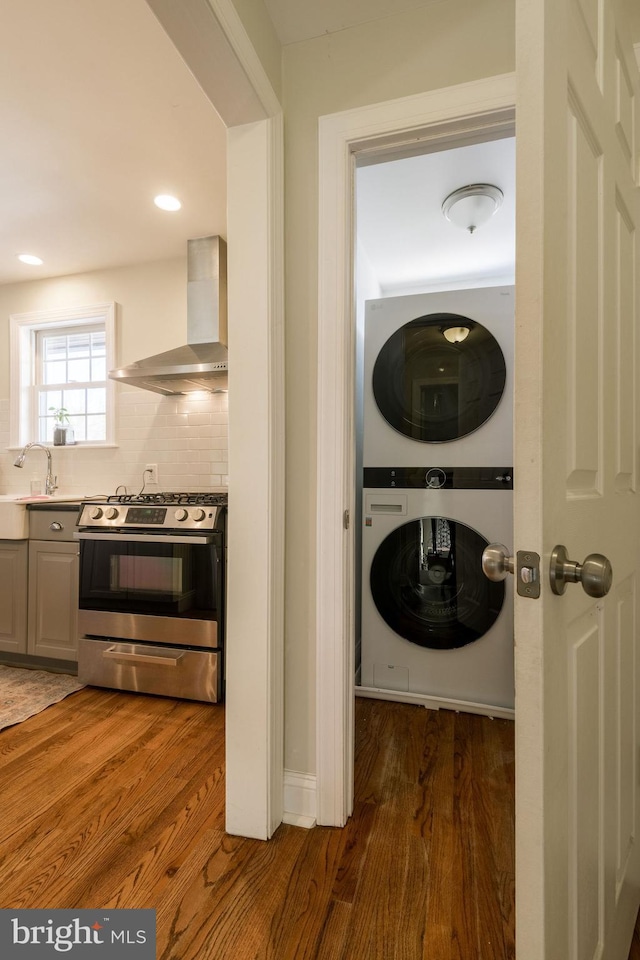 clothes washing area featuring stacked washer and dryer, dark hardwood / wood-style flooring, and sink