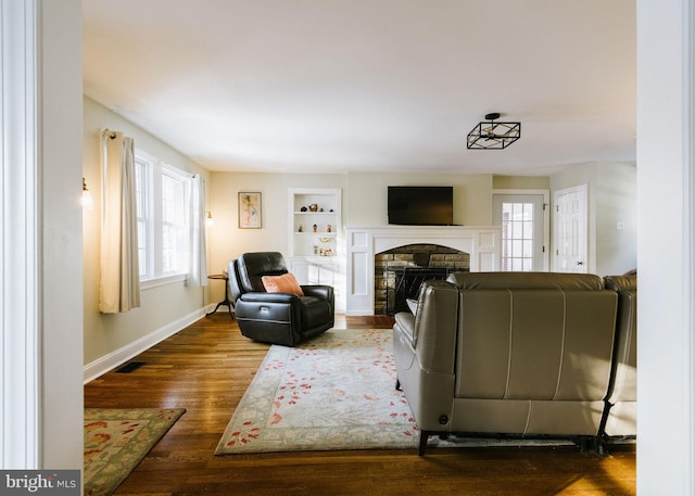 living room with a stone fireplace, dark hardwood / wood-style floors, and built in shelves