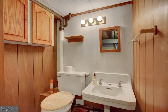 bathroom with toilet, sink, a textured ceiling, and wood walls