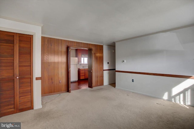 unfurnished bedroom with crown molding, wooden walls, white refrigerator, light carpet, and a closet