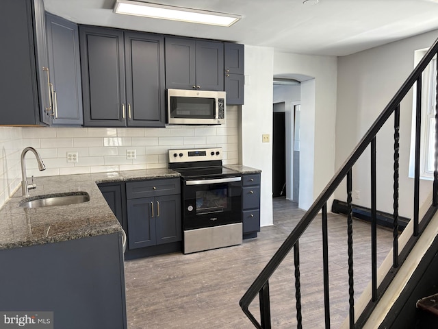 kitchen featuring sink, dark stone countertops, stainless steel appliances, light hardwood / wood-style floors, and decorative backsplash