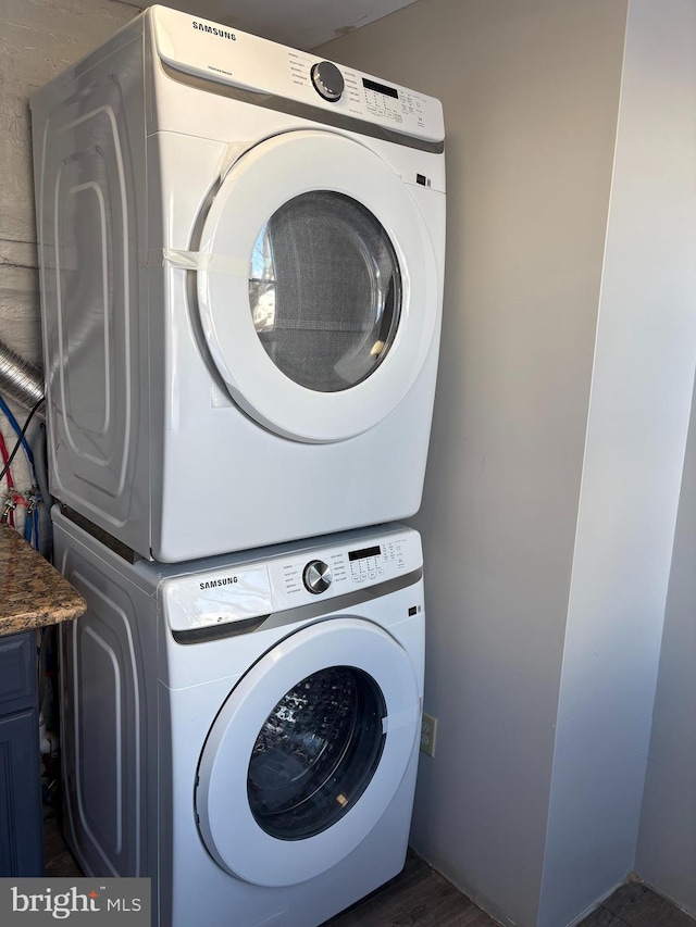 laundry room with dark hardwood / wood-style flooring, stacked washer / drying machine, and cabinets