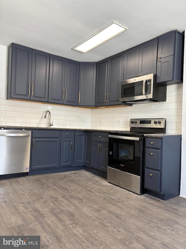 kitchen with stainless steel appliances, sink, wood-type flooring, and dark stone counters