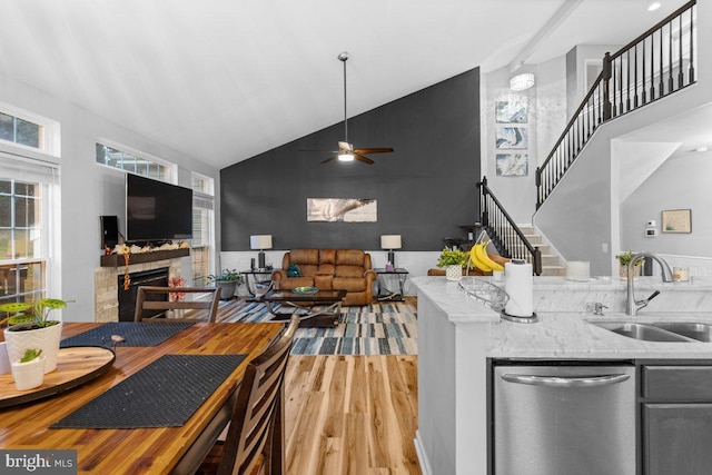 kitchen featuring high vaulted ceiling, dishwasher, sink, hardwood / wood-style flooring, and light stone countertops