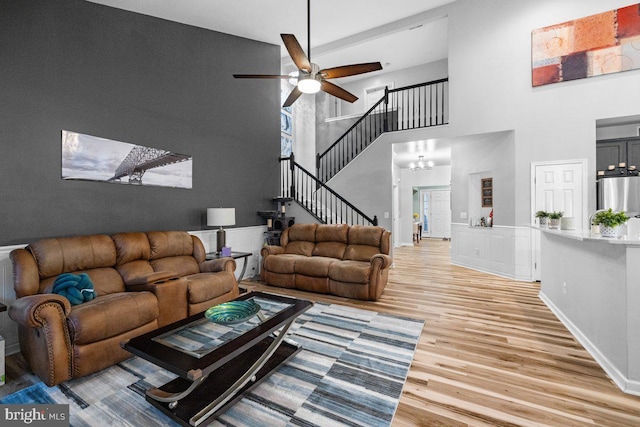 living room featuring hardwood / wood-style floors, ceiling fan with notable chandelier, and a towering ceiling