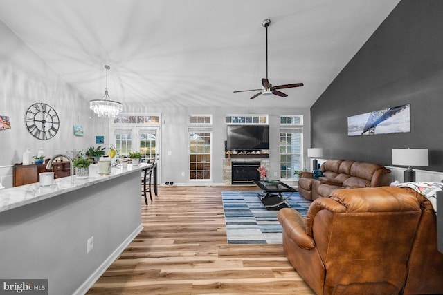 living room featuring lofted ceiling, ceiling fan with notable chandelier, and light wood-type flooring