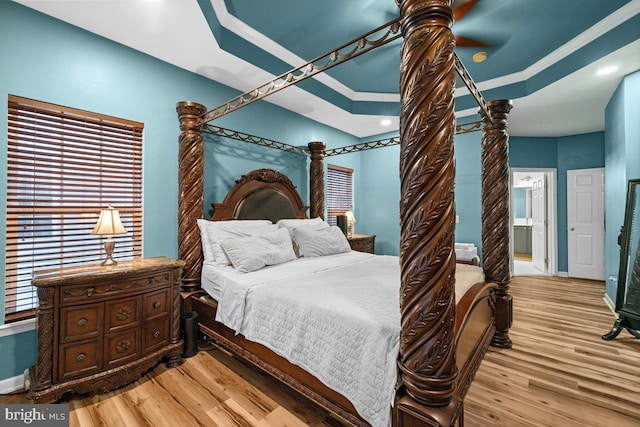 bedroom with ensuite bath, ornamental molding, light hardwood / wood-style floors, and a raised ceiling