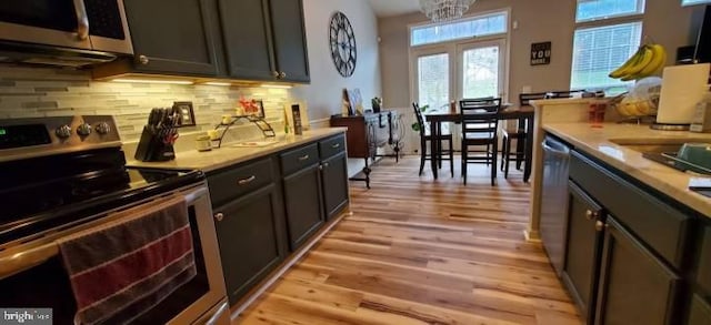 kitchen featuring backsplash, light hardwood / wood-style flooring, a chandelier, and appliances with stainless steel finishes