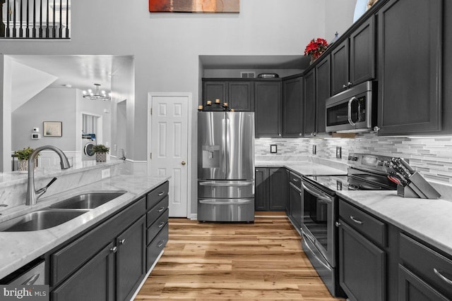 kitchen featuring sink, appliances with stainless steel finishes, light stone countertops, light hardwood / wood-style floors, and decorative backsplash