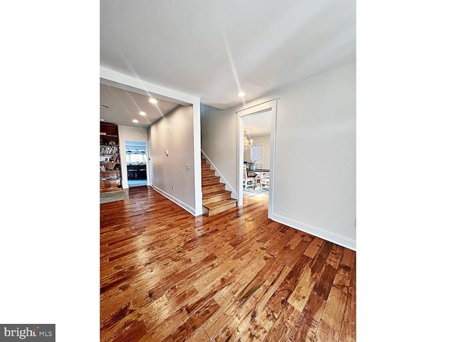 unfurnished room featuring recessed lighting, wood finished floors, baseboards, and stairs