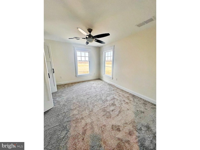 carpeted empty room with baseboards, visible vents, and ceiling fan