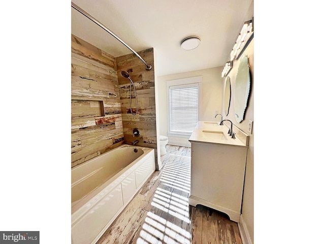 bathroom featuring shower / bathtub combination, toilet, wooden walls, vanity, and wood finished floors