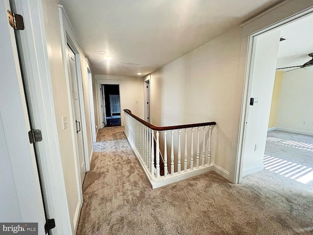 hall with carpet floors, baseboards, and an upstairs landing