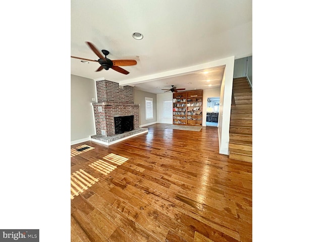 unfurnished living room featuring baseboards, a ceiling fan, stairway, hardwood / wood-style floors, and a fireplace