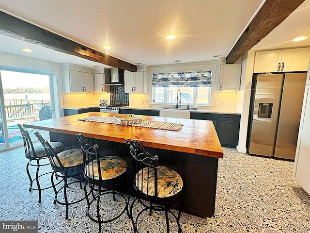 kitchen featuring stainless steel appliances, a sink, wood counters, beamed ceiling, and wall chimney exhaust hood