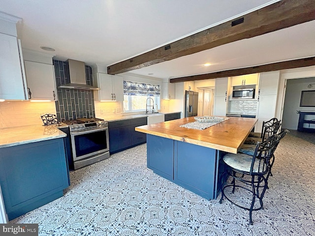 kitchen with a breakfast bar area, wood counters, appliances with stainless steel finishes, blue cabinetry, and wall chimney exhaust hood