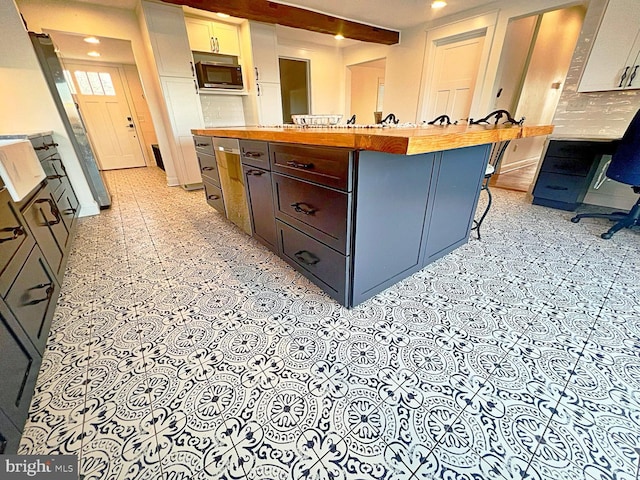 kitchen featuring white cabinets, a large island, wood counters, stainless steel microwave, and a kitchen bar