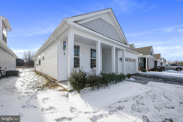 snow covered property featuring a garage and central AC