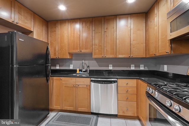 kitchen with light tile patterned floors, stainless steel appliances, sink, and dark stone counters