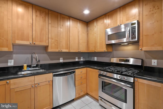 kitchen featuring dark stone countertops, stainless steel appliances, sink, and light tile patterned floors