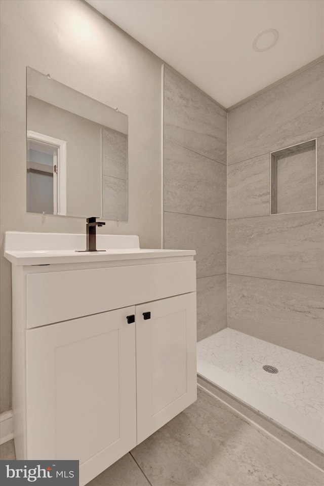 bathroom with a tile shower, vanity, and tile patterned flooring