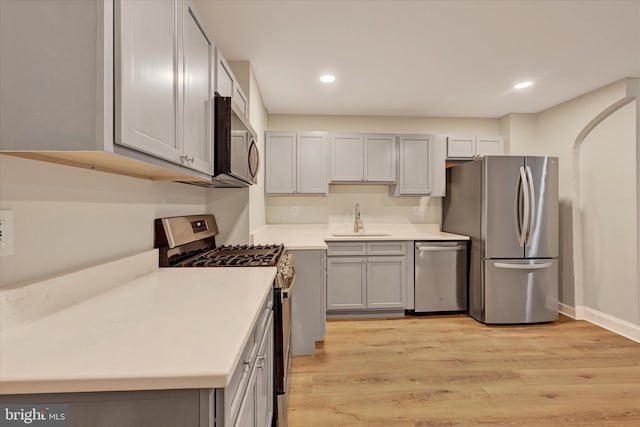 kitchen with appliances with stainless steel finishes, sink, gray cabinetry, and light hardwood / wood-style flooring