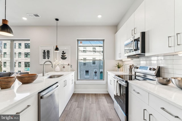 kitchen featuring sink, decorative light fixtures, white cabinets, stainless steel appliances, and backsplash