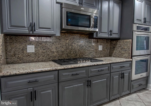 kitchen featuring stainless steel appliances, light stone countertops, decorative backsplash, and gray cabinetry