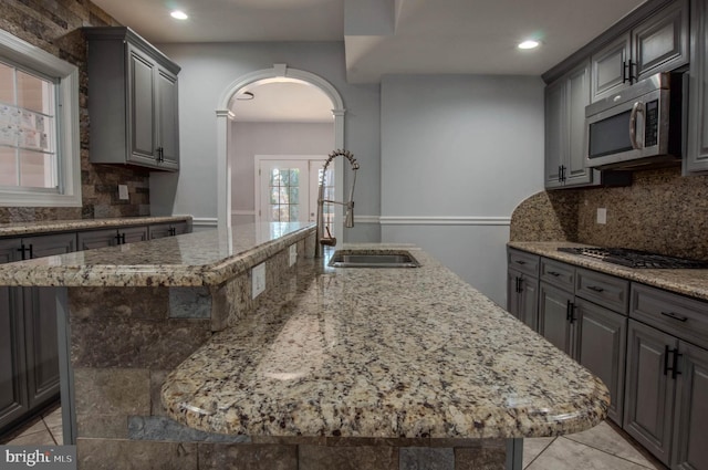 kitchen with sink, light stone counters, appliances with stainless steel finishes, gray cabinets, and a kitchen island