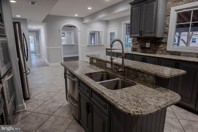 kitchen with light stone counters, sink, tasteful backsplash, and a center island with sink