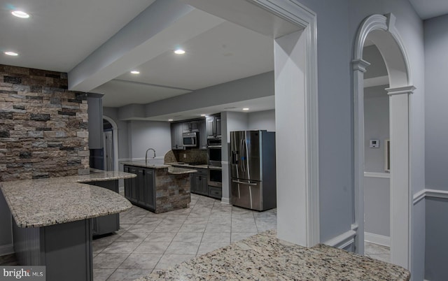 kitchen with ornate columns, a center island, kitchen peninsula, stainless steel appliances, and light stone countertops